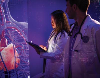 Two Case Western Reserve University medical students stand in a dark room looking at a hologram of a body on a wall