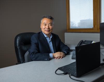 Photo of person sitting at desk with computers, smiling at camera
