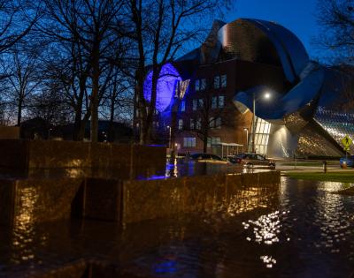 Photo of the Peter B. Lewis Building at night with lights reflecting off it and the water in the Merging sculpture in the foreground
