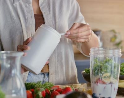 Close up photo of a woman adding protein powder to a smoothie