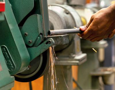 Close-up of a person using a green bench grinder with sparks flying. 