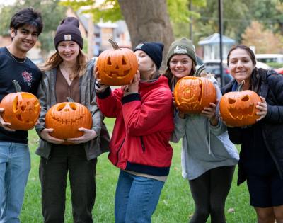 A group of happy students hold jack-o-lanterns. 