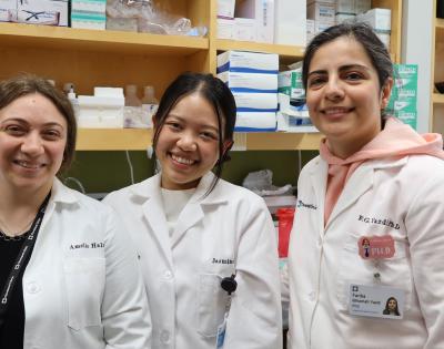 Three people in lab coats smiling in a laboratory setting. Shelves with lab supplies are in the background. 