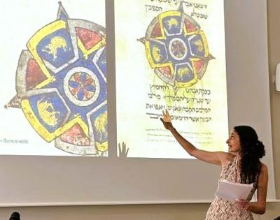 Photo of Elina Gertsman presenting at a symposium with the cover of her book on abstraction in medieval art projecting on the wall