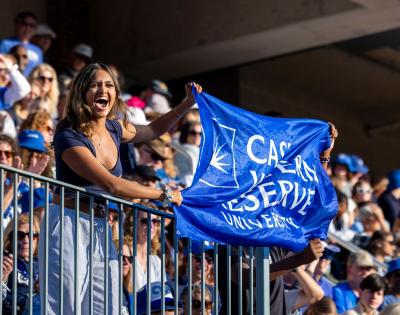 Excited member of the CWRU community holds a CWRU flag at a football game during Homecoming and Reunion weekend.