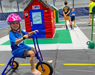 Photo of a child wearing a helmet riding a tricycle on a model town set up for CWRU's Safety Town