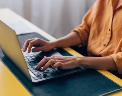Close up of an individual typing on a laptop at a desk.