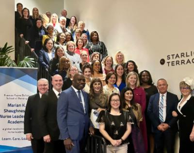 A large group of people poses on a staircase by a sign for the arian K. Shaughnessy Nurse Leadership Academy. 