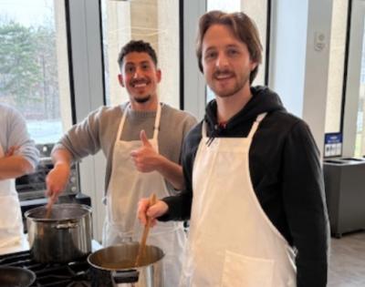 three students smiling together while cooking in the teaching kitchen