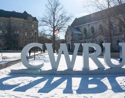 Photo of the CWRU letters on a snowy day with Adelbert Hall and Amasa Stone Chapel behind them