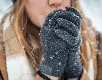 Close up of a woman blowing on her hands to warm them in the cold weather.