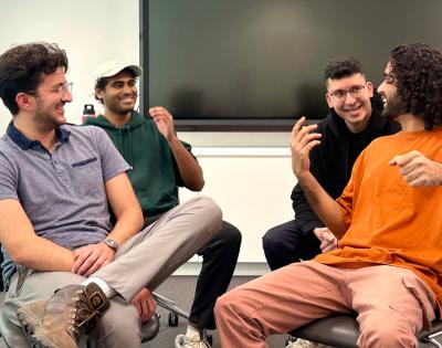 four medical students sitting in chairs, laughing with each other as they act out an improv sketch