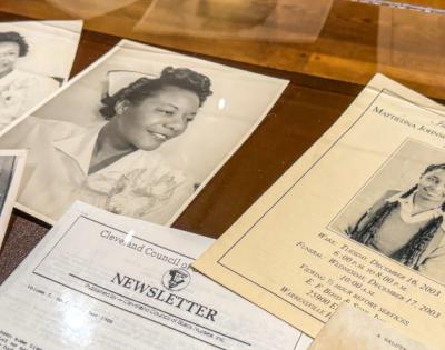 A selection of papers feature photos of Black nurses are spread out in a display case.