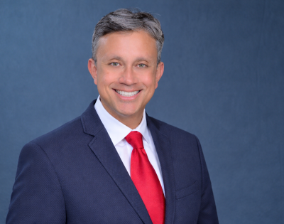 Andres Pinto poses in a blue jacket and red tie in front of a blue background.