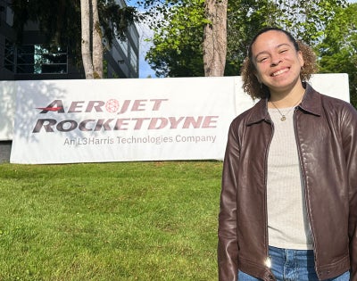 Photo of Andrea Silva posing for a photo in front of the Aerojet Rocketdyne sign during an internship