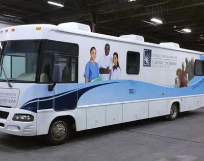 The white and blue CWRU dental clinic bus sits in a garage.
