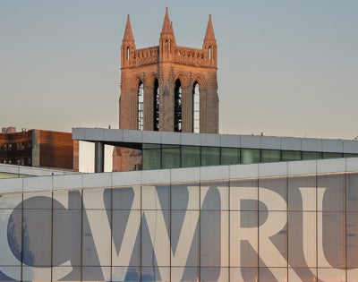 Photo of the CWRU letters covering the windows in Tinkham Veale University Center with the Church of the Covenant bell tower in the background