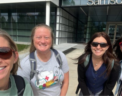Four women smile at the camera in front of Samson Pavilion.