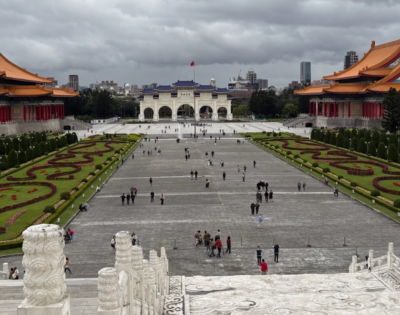 A view from the Chiang Kai Shek memorial Hallof an elaborate garden and walkway with orange-roofed buildings against a cloudy sky.