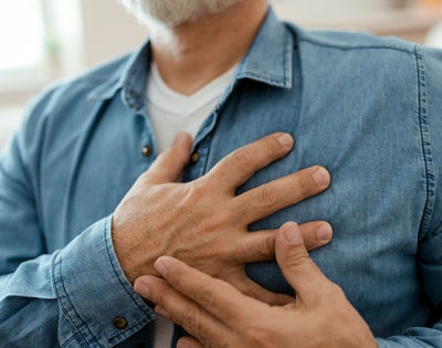 Close up photo of a man clutching his chest over his heart with both hands