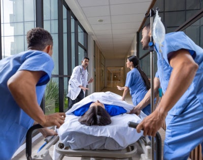 Healthcare workers rushing a patient in a gurney to the emergency room 
