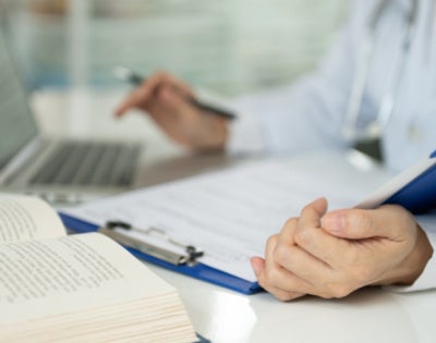 An unidentified person wearing a stethoscope writes in a book