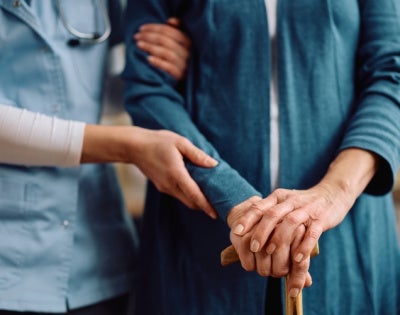 Close up of nurse and senior woman with walking cane during home visit. 