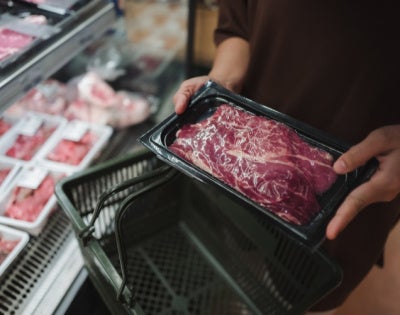 Hands hold raw meat package at a grocery store 