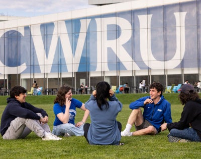 Five students sit in front of large “CWRU” signage on Freiberger Field.