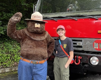 Meg Corley standing with Smokey the bear in front of a truck