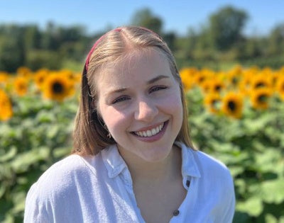 Julie Somogyi poses for a photo in front of a field of sunflowers