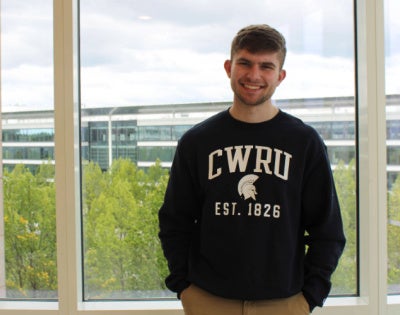 Jacob Hoffa stands in front of a window in front of Samson Pavilion wearing a CWRU sweatshirt.