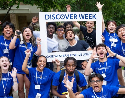 A large group of orientation leaders and student move-in volunteers gather for a photo during move-in weekend posing with a photo frame that says "Discover Week Case Western Reserve University"