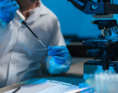 Photo of lab researcher with microscope and slide.