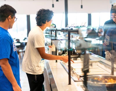 Students at the counter of a CWRU dining hall as a smiling employee prepares to serve them food