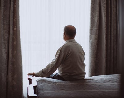 Photo of an elderly man sitting alone on a bed in a darkened room