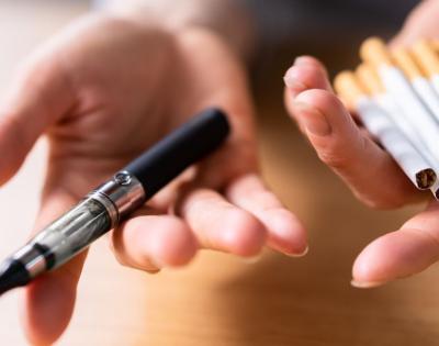 Hand Holding Vape And Tobacco Cigarettes Over Wooden Desk