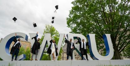Five students stand in front of the CWRU sign and throw their commencement hats in the air