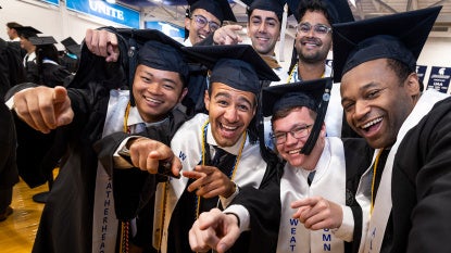 A group of students stand together in commencement regalia for a fun photo