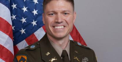 Person wearing military uniform, smiling in front of American flag