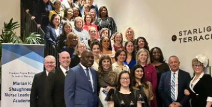 A large group of people poses on a staircase by a sign for the arian K. Shaughnessy Nurse Leadership Academy. 