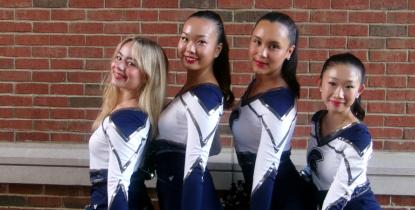 Four members of the CWRU Dance Team pose in their uniforms in front of a brick wall.