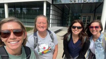 Four women smile at the camera in front of Samson Pavilion.