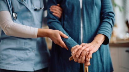 Close up of nurse and senior woman with walking cane during home visit. 