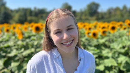 Julie Somogyi poses for a photo in front of a field of sunflowers
