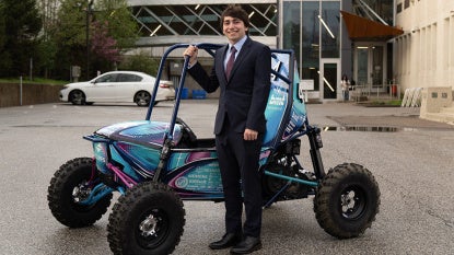 David Kaplan poses for a photo in a suit and tie with the CWRU Baja vehicle