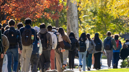 A line of students walk on the CWRU campus with a color-changing trees in the background. 