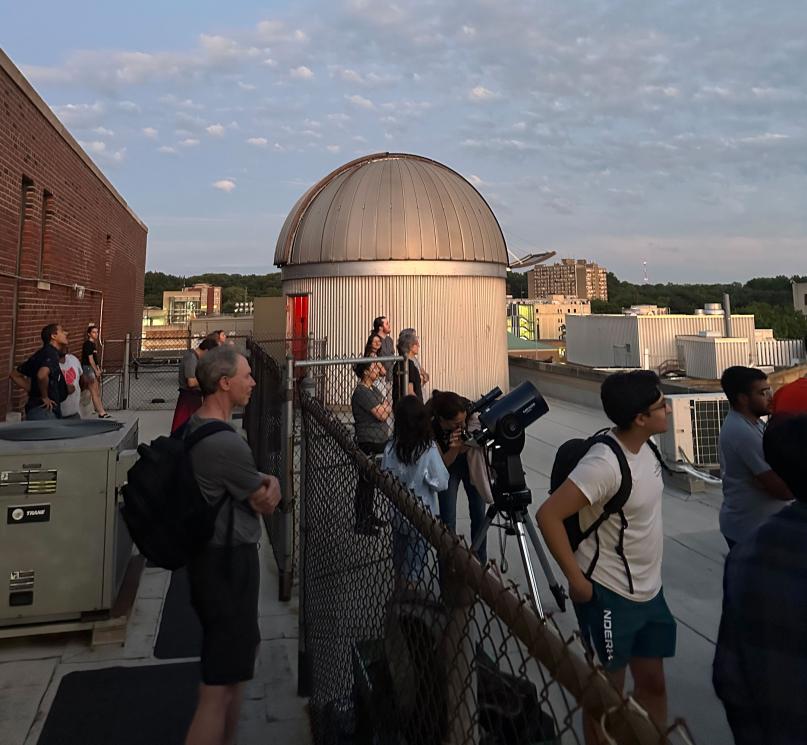Members of the CWRU community on a roof, looking at the sky near the AW Smith Rooftop Telescope.