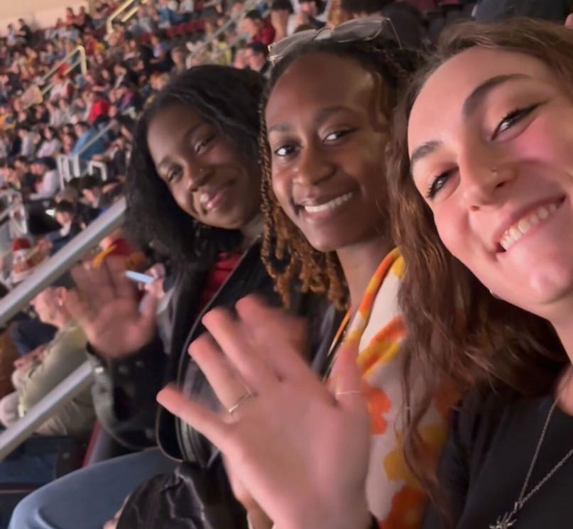 Three students waving at the camera in the stands at Rocket Arena. 