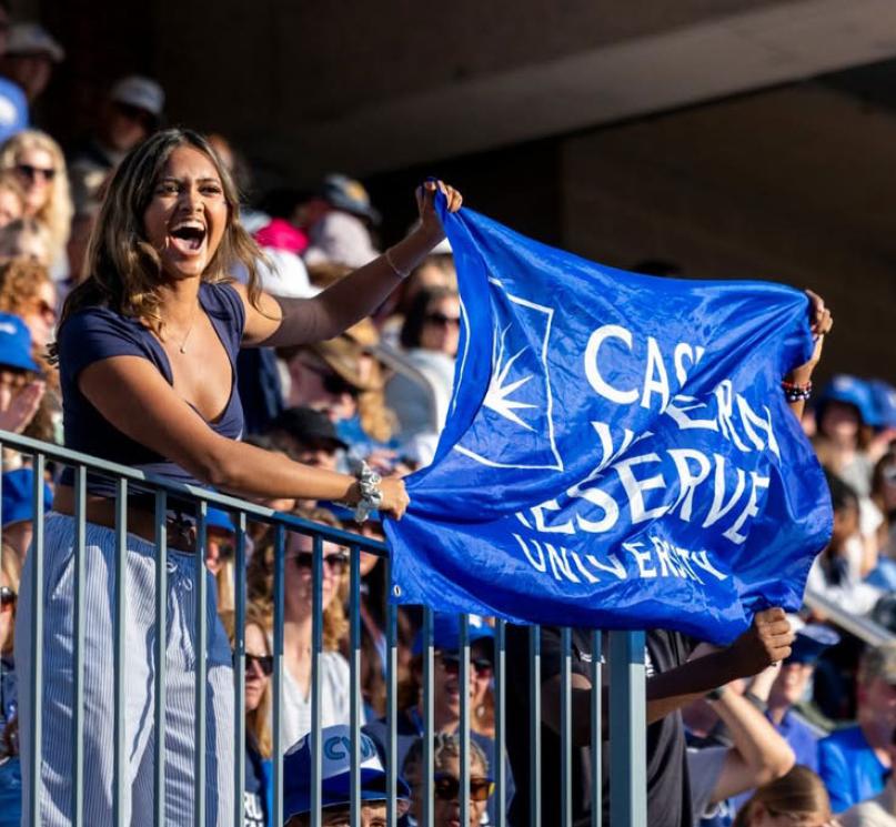 Student holding a flag that reads, “Case Western Reserve University," in the crowded stands of DiSanto Field.